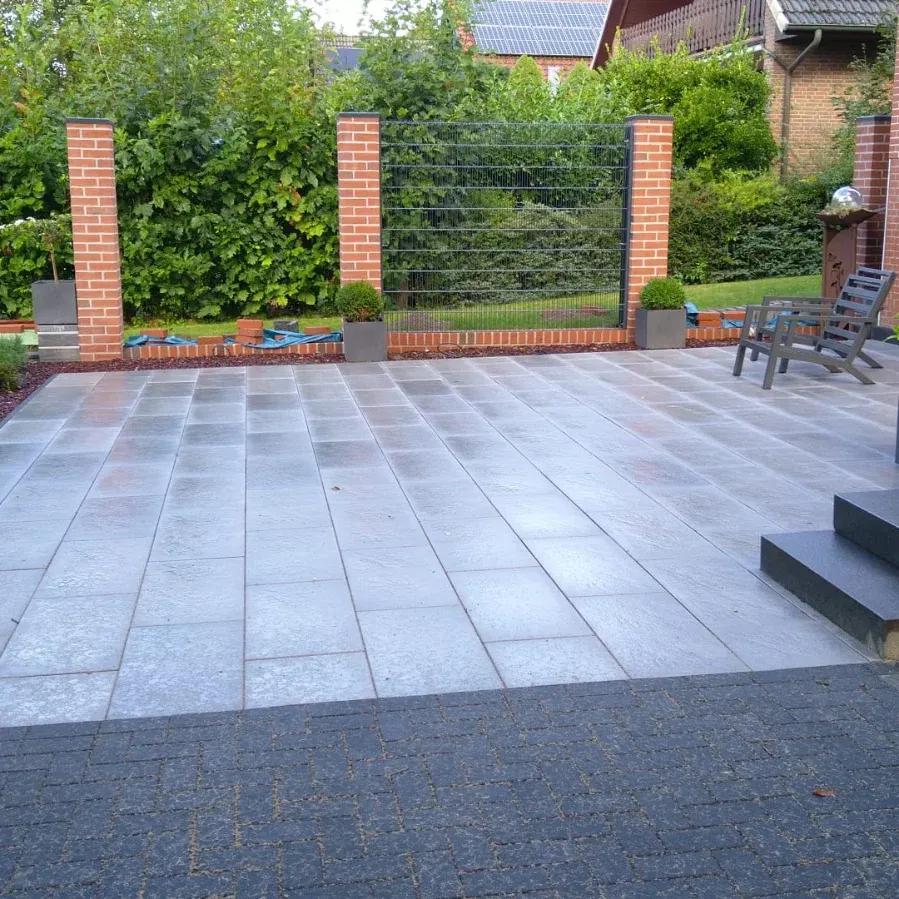 Neu verlegte Terrasse aus großformatigen Platten mit gemauerten Klinkersäulen und Zaunfeldern